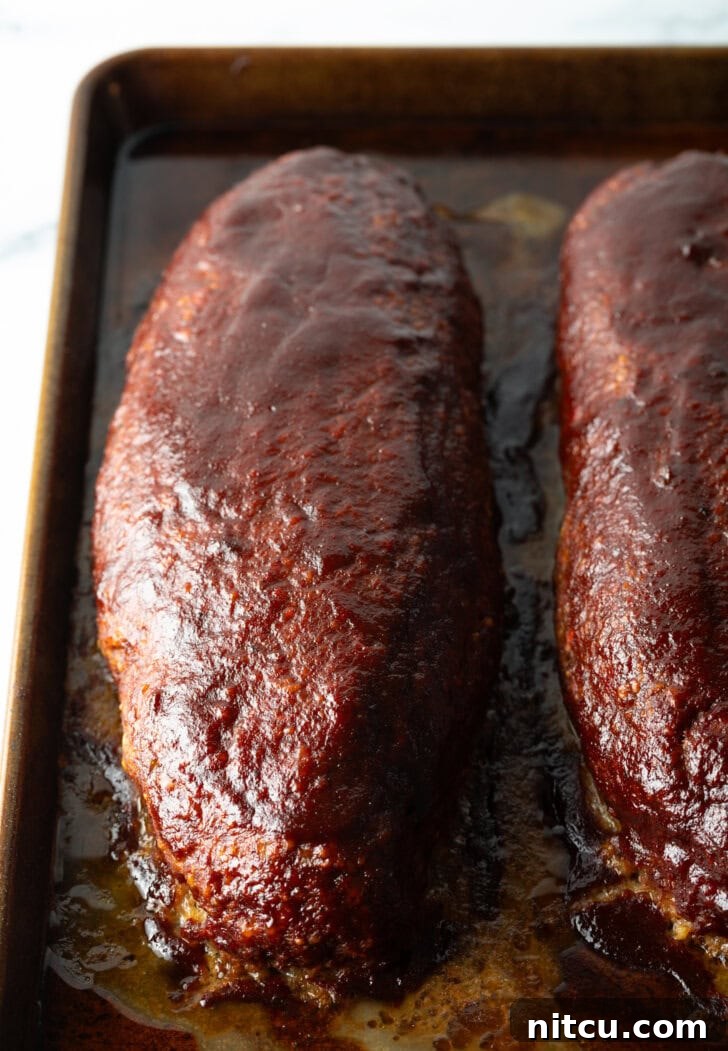 A top-down shot of two perfectly cooked and glazed meatloaves resting after being removed from the smoker, showcasing their rich color and inviting aroma.