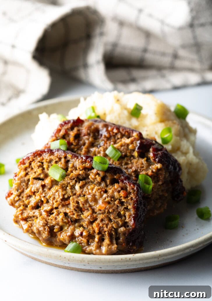 Two slices of smoked meatloaf resting on a plate, accompanied by a generous serving of mashed potatoes, and garnished with vibrant chopped green onions for a fresh finish.