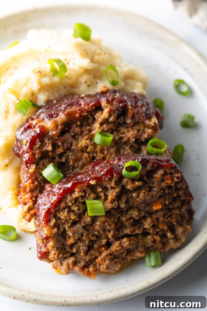 Two slices of tender, moist smoked meatloaf, artfully placed on a plate with a dollop of creamy mashed potatoes and a sprinkle of fresh green onions, ready to be enjoyed.