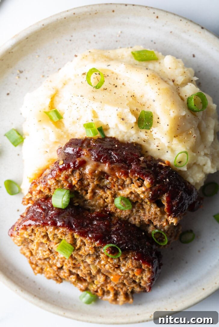 Two beautiful slices of smoked meatloaf arranged on a plate next to a fluffy portion of mashed potatoes, with a sprinkle of fresh green onions adding a pop of color and freshness.