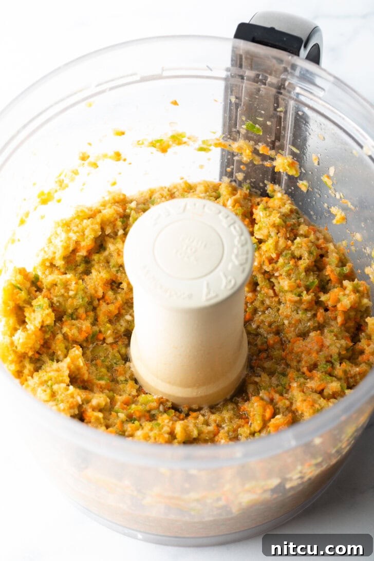 A large mixing bowl filled with ground beef, minced vegetables, and various spices, poised for the hand-mixing stage of the meatloaf preparation.