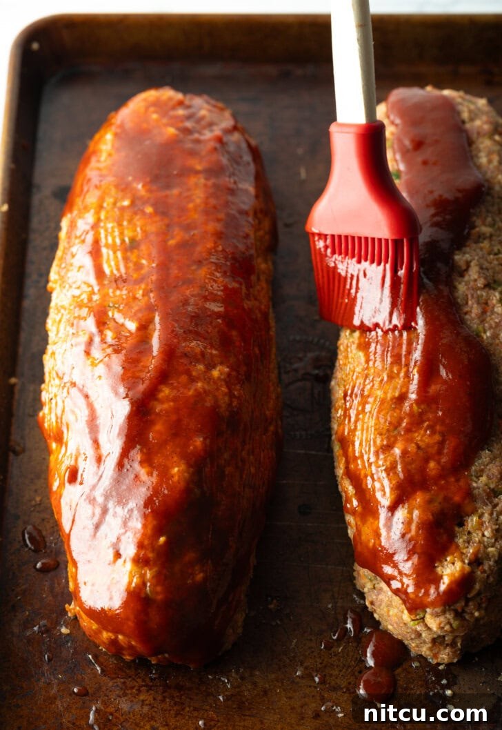 A close-up view emphasizing the careful application of barbecue sauce to the surface of the raw meatloaf, ensuring a flavorful glaze.