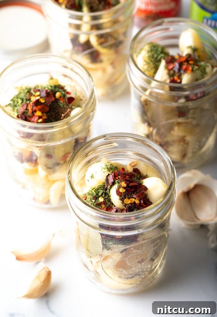 Top down open glass jar stuffed with preserved garlic and herbs.