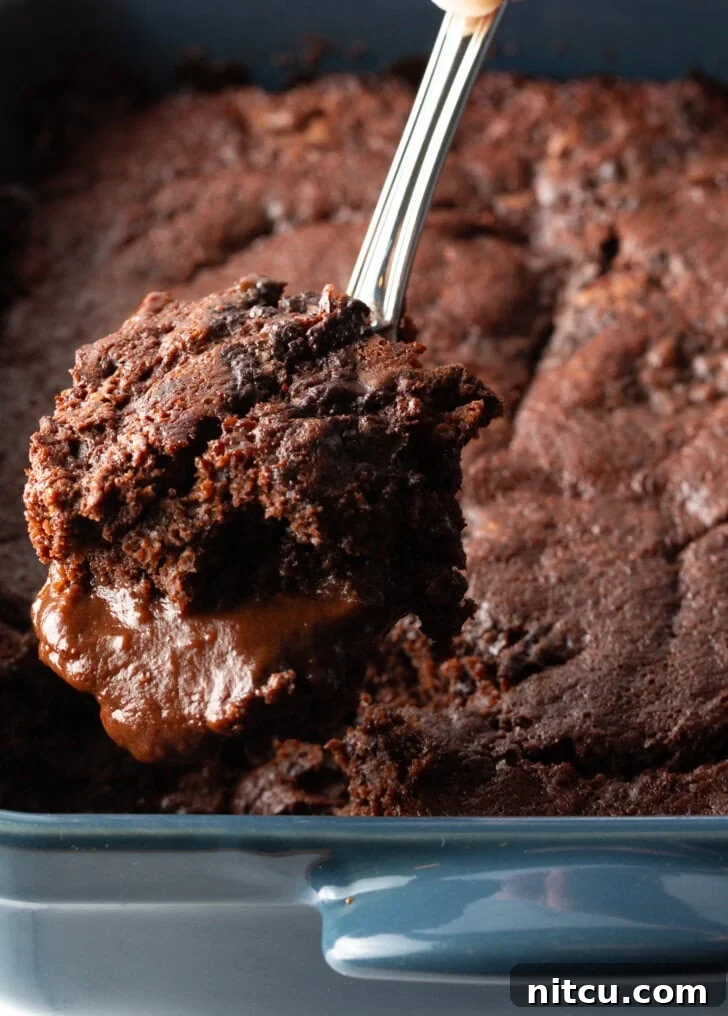 Hand using a metal spoon to scoop a serving of pudding cake from the baking pan.