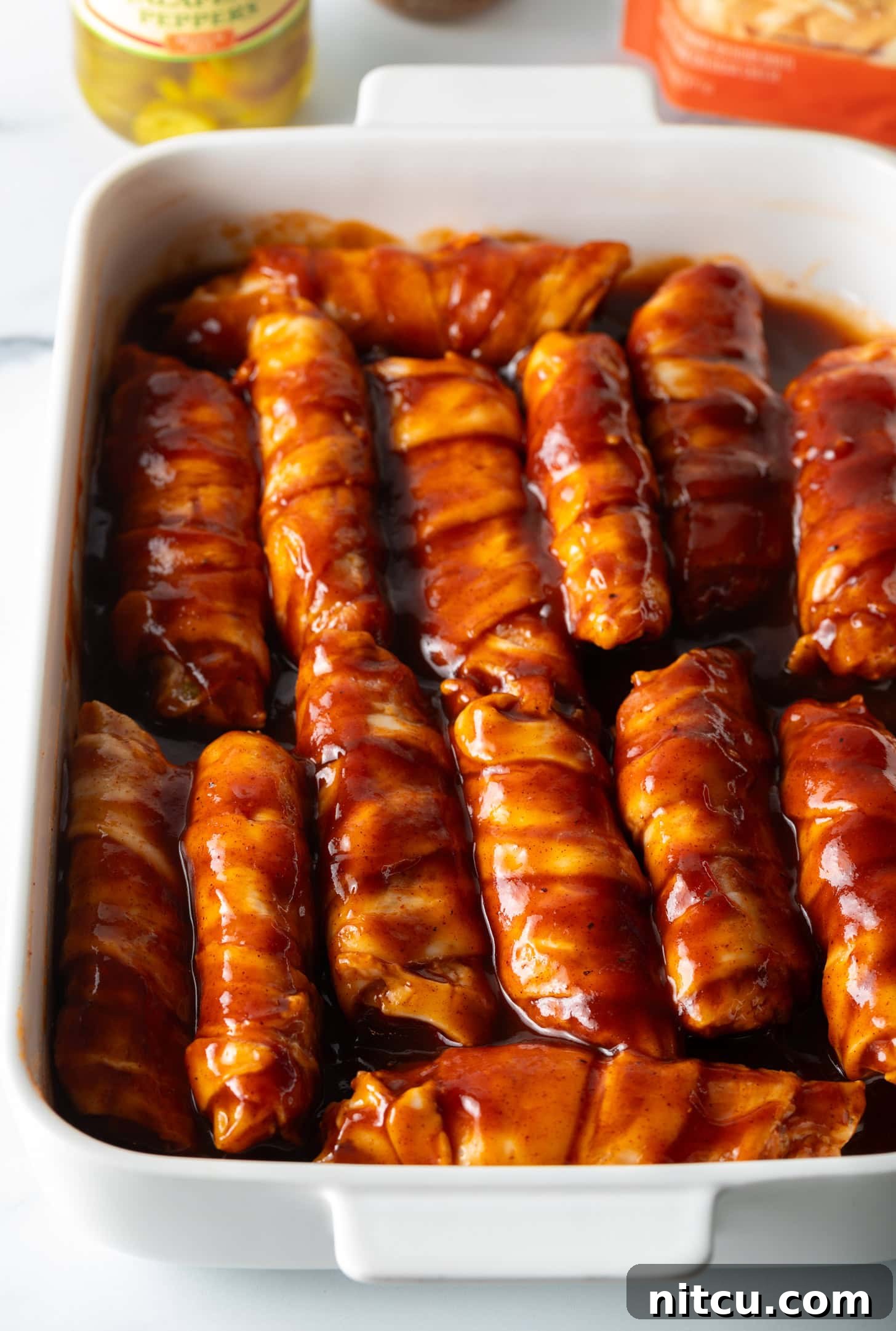 White baking dish filled with raw stuffs shells, all coated in bbq sauce.