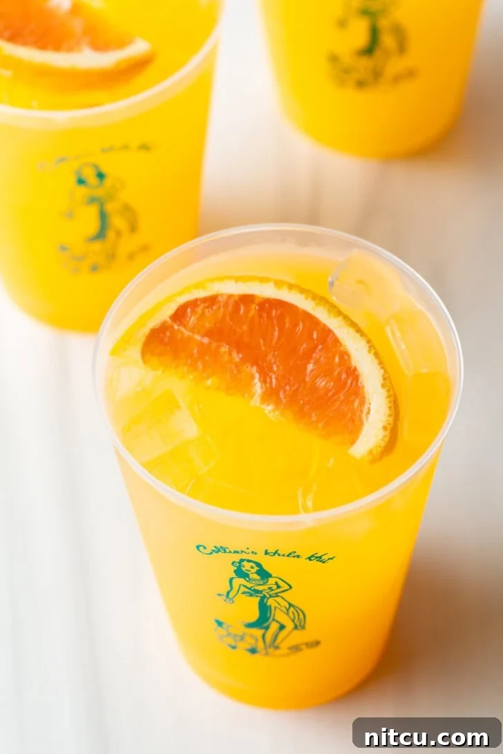 Top-down view of three Sunny D Vodka Seltzer drinks, each in a glass cup with a slice of orange on top.