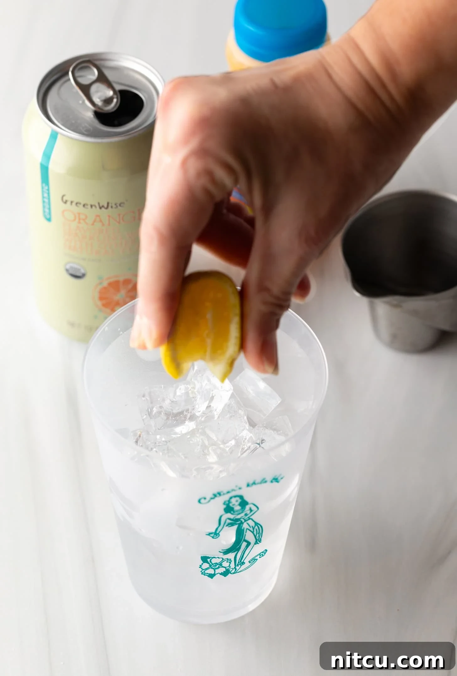 Hand squeezing orange juice into a glass filled with ice.