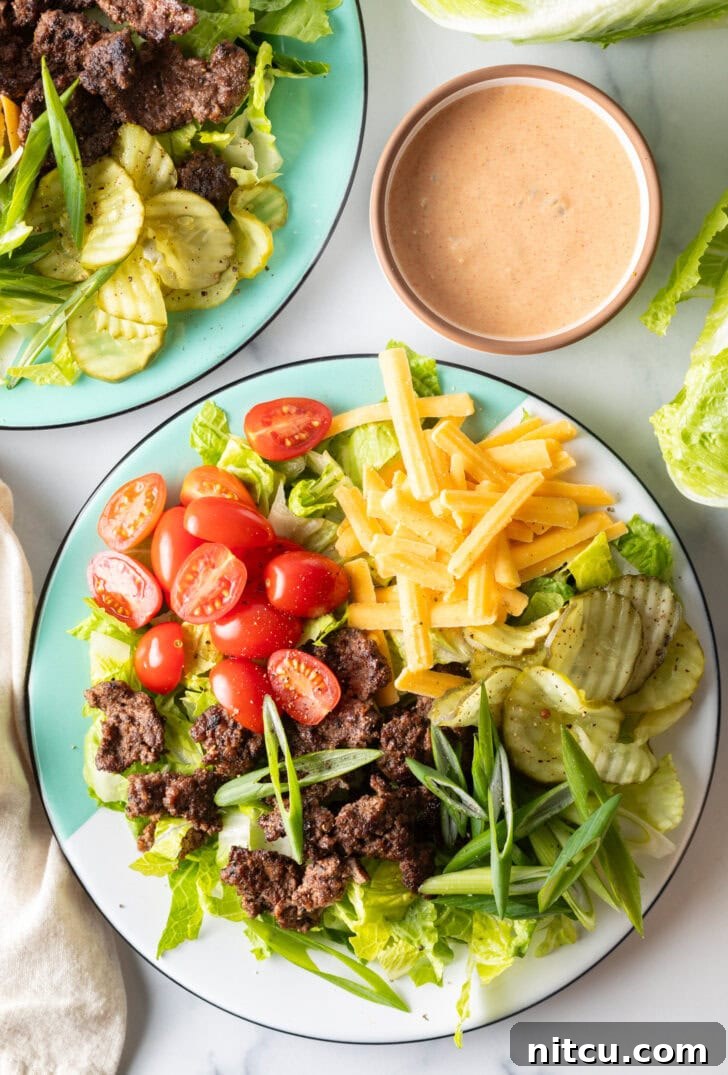 A vibrant, loaded Big Mac cheeseburger salad featuring crisp shredded lettuce, seasoned ground beef crumbles, juicy halved grape tomatoes, rich shredded cheddar cheese, crunchy dill pickles, and fresh sliced green onion, ready for enjoyment.