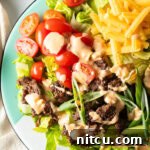 A hearty Big Mac burger salad with shredded lettuce, ground beef, halved grape tomatoes, shredded cheese, pickles, and sliced green onion, all topped with a drizzle of Thousand island dressing.