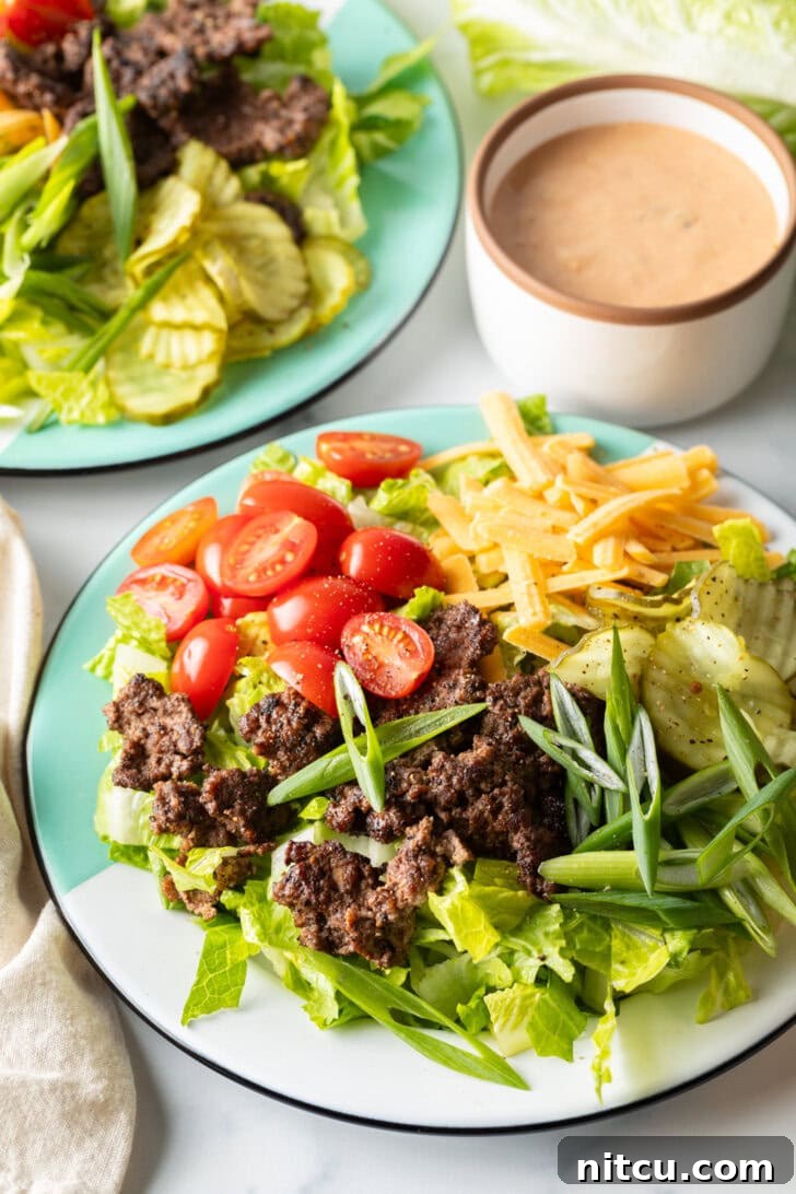 A beautifully arranged Big Mac cheeseburger salad with fresh shredded lettuce, perfectly browned ground beef crumbles, halved grape tomatoes, rich shredded cheese, zesty pickles, and thinly sliced green onion.