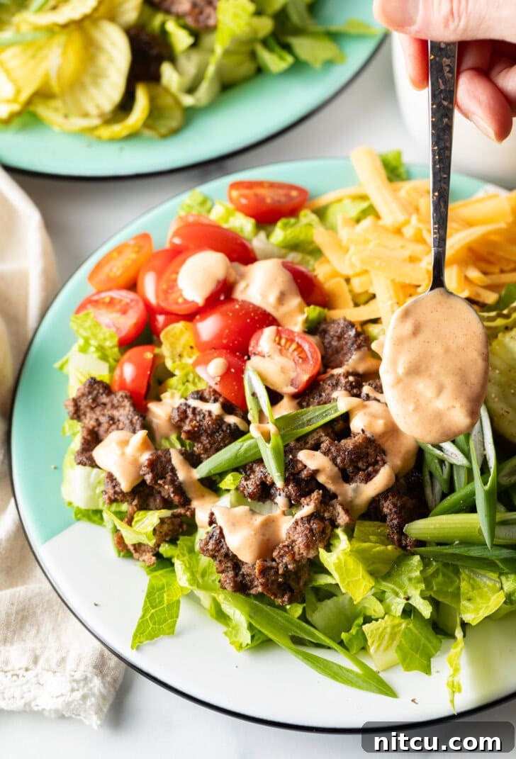 A close-up shot of creamy, orange-hued Big Mac sauce being expertly drizzled from a spoon over a fresh, vibrant burger salad, highlighting its rich texture.