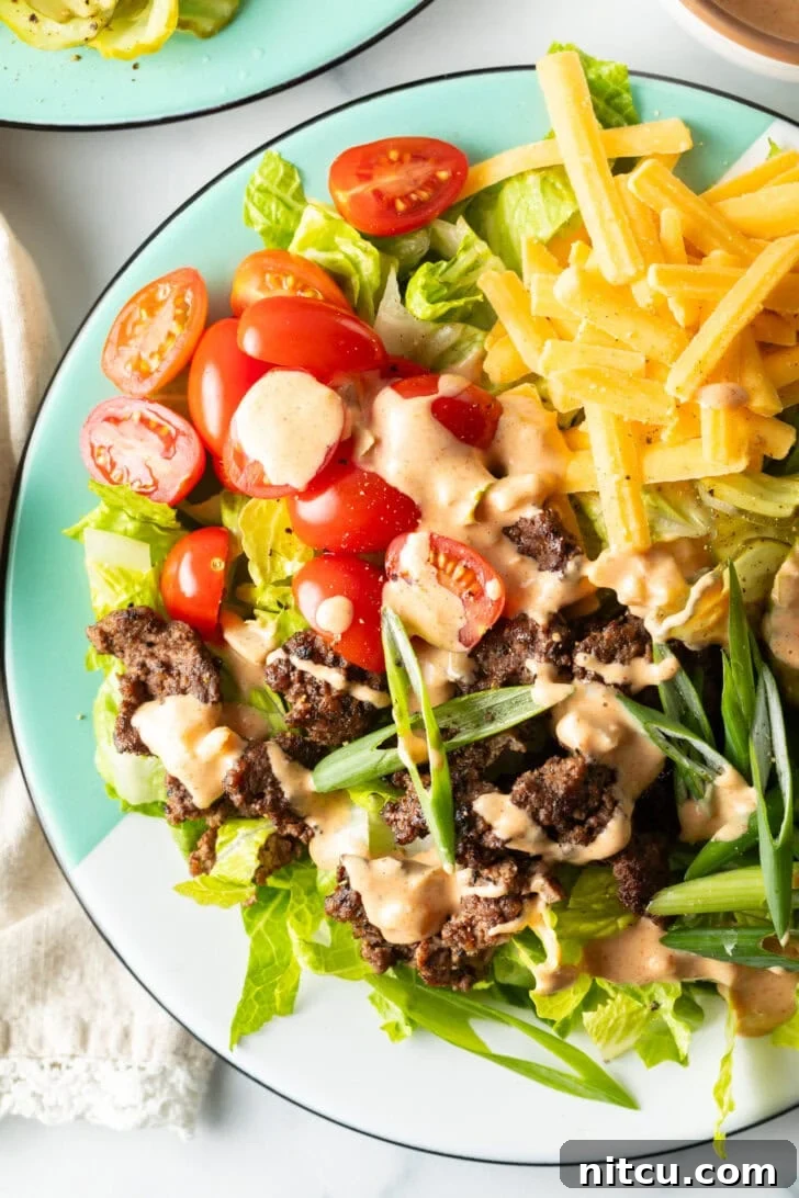 A generous Big Mac burger salad featuring crisp shredded lettuce, savory ground beef crumbles, sweet halved grape tomatoes, rich shredded cheese, tangy pickles, and fresh sliced green onion, all exquisitely drizzled with Thousand Island dressing.