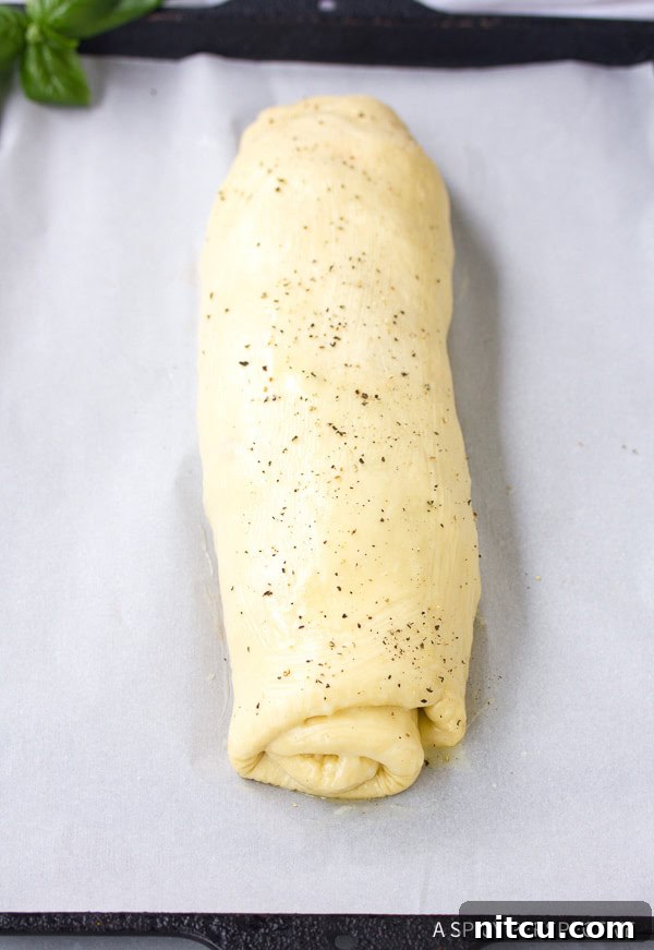 A perfectly rolled Stromboli log on parchment paper, brushed with butter and sprinkled with pepper, ready for baking.