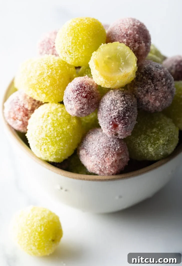 A bowl of green and purple candy grapes. One of the green grapes has been bitten in half to show the inside.