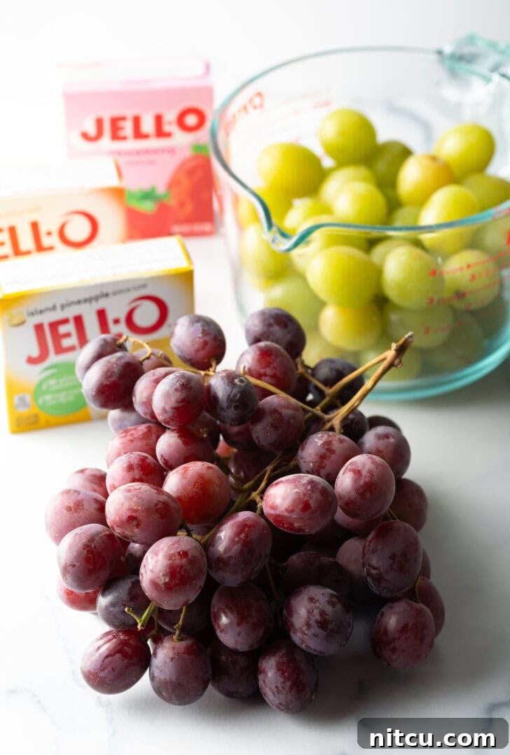 Recipe ingredients: a bunch of red grapes in the front view, in the background is a large glass measuring cup with green grapes. 3 boxes of Jello are to the side.