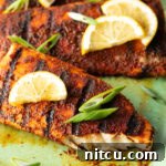Close view of a fillet of grilled mahi mahi topped with a slice of lemon and green onions. A bite has been removed from the fish to show the white flaky inside of the meat.