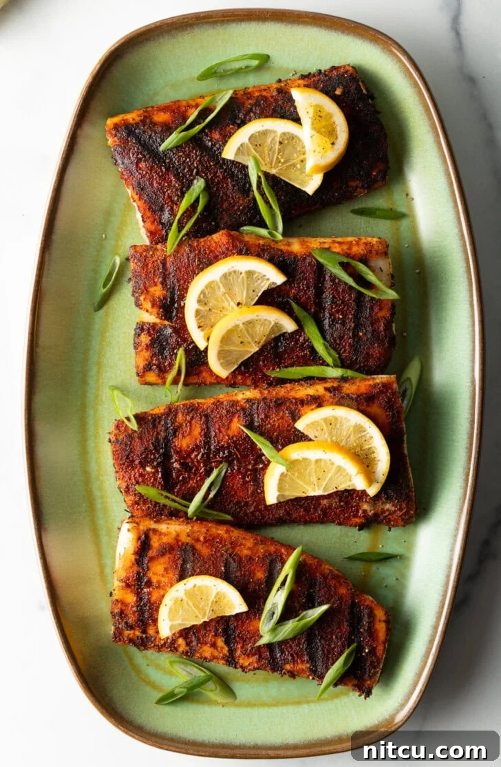 Top down view of 4 pieces of blackened and grilled fish, all topped with slices of lemon and green onions.