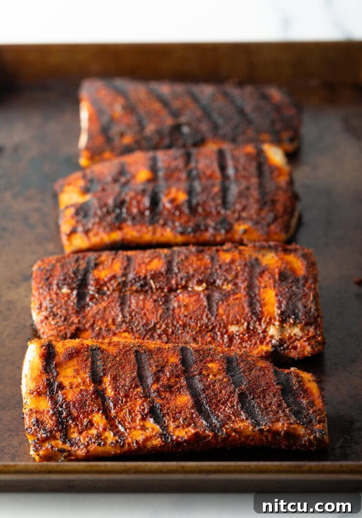 4 large fillets of grilled fish on a baking sheet coated with blackening seasoning.