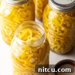 Four jars of homemade pickled banana peppers, with one open jar showing sliced peppers.