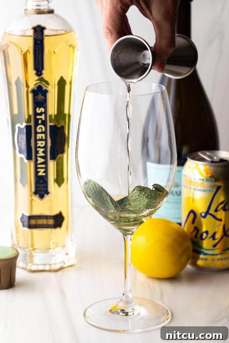 Hand adding liquor from a metal shot glass on top of the muddled mint leaves.