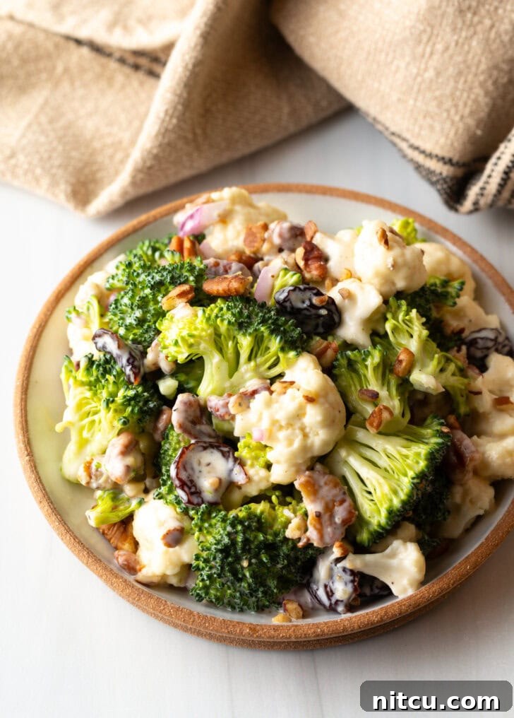Bowl of crisp broccoli and cauliflower salad, beautifully tossed with crunchy pecans, vibrant red onions, and sweet dried cranberries, ready to be served.