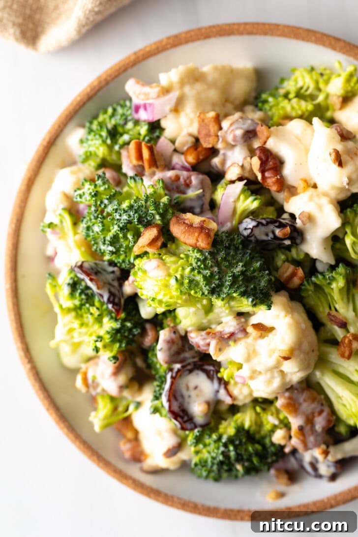 Top down view of a large bowl filled with vibrant broccoli and cauliflower salad, showcasing its fresh ingredients and creamy dressing.