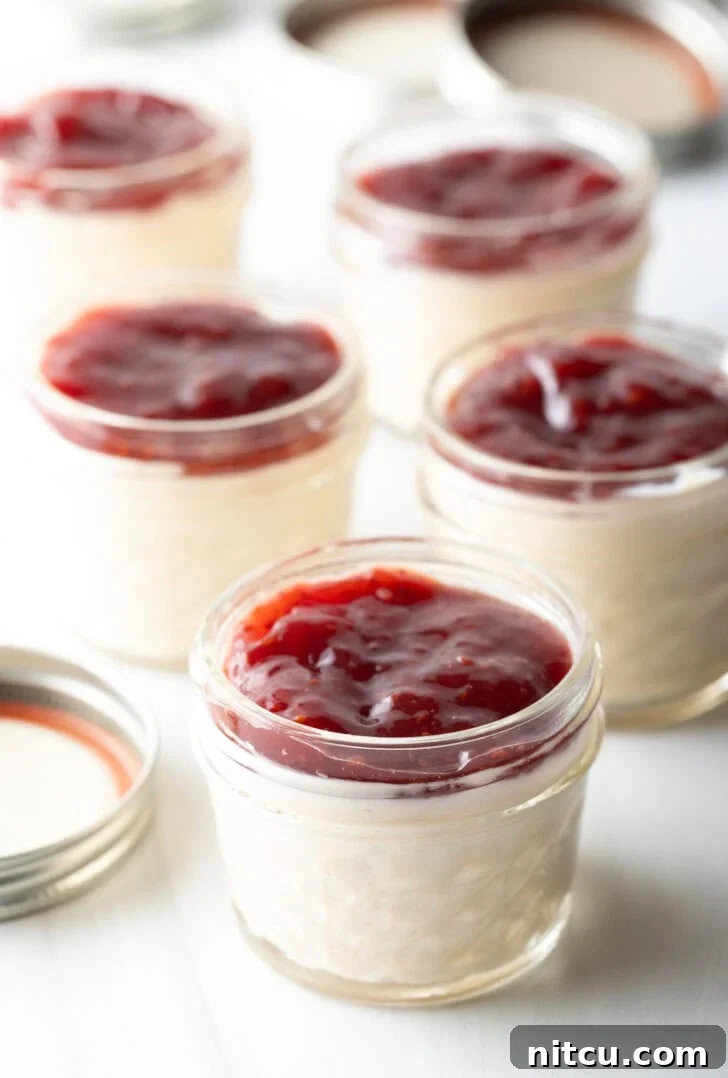 5 small glass jars of protein pudding topped with raspberry jam.