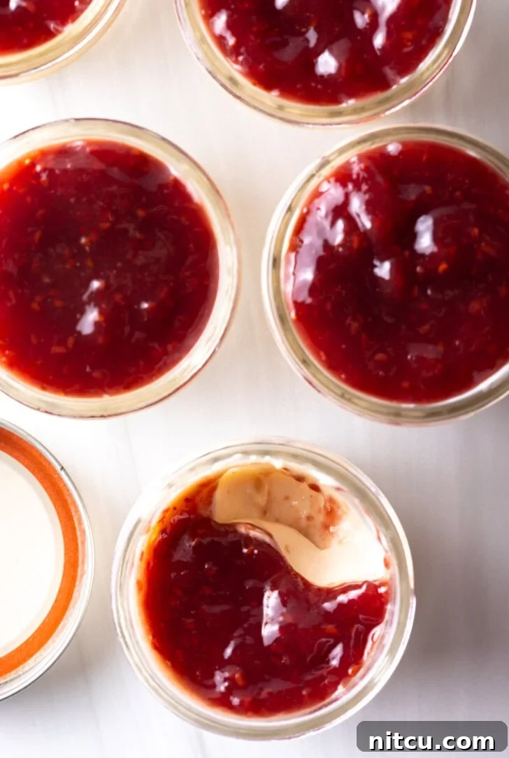 Top down view of 4 glass jars of protein yogurt topped with raspberry jam.