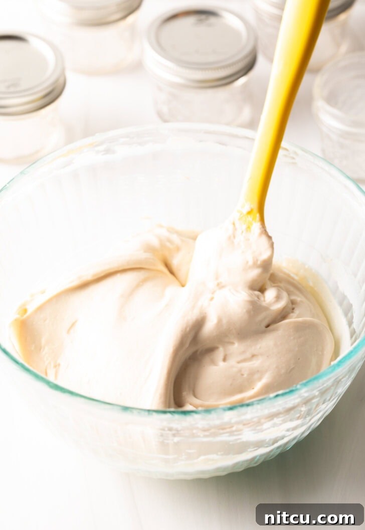 Glass bowl with homemade protein yogurt being whipped with a yellow spatula.