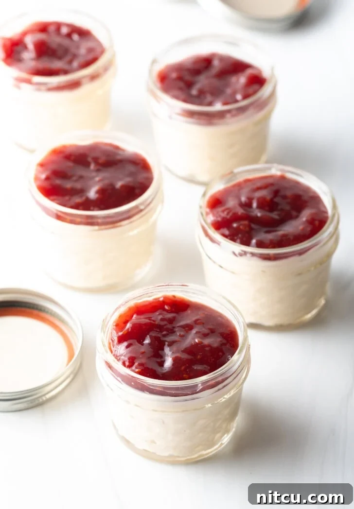 5 small glass jars of protein pudding topped with raspberry jam.