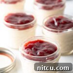 5 small glass jars of protein pudding topped with raspberry jam.
