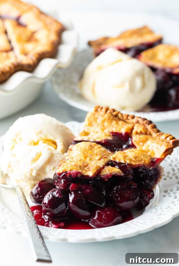 A delectable slice of homemade cherry pie, perfectly baked with a golden crust, served on a white plate alongside a scoop of creamy vanilla ice cream, promising a delightful dessert experience.
