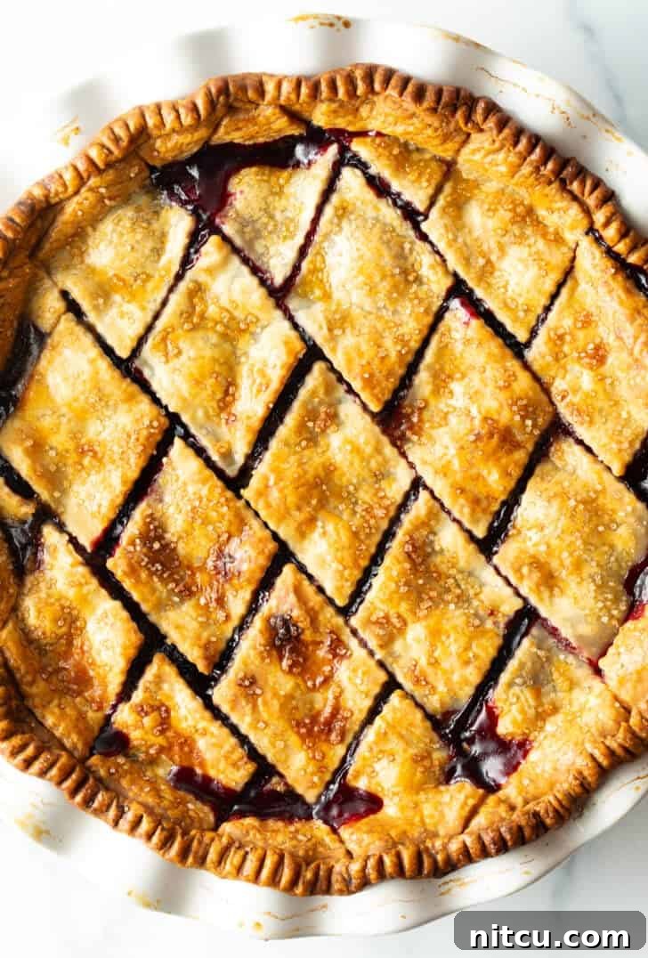 A freshly baked cherry pie with a golden, diamond-patterned crust, showcasing its perfect golden-brown finish after coming out of the oven.