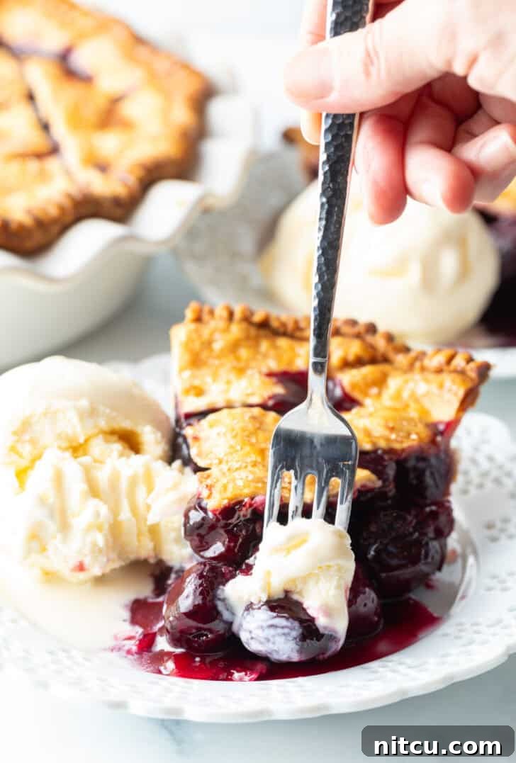 A close-up of a bite of the best homemade Cherry Pie recipe, revealing the rich filling and flaky crust, with a dollop of vanilla ice cream melting on the side, highlighting its deliciousness.
