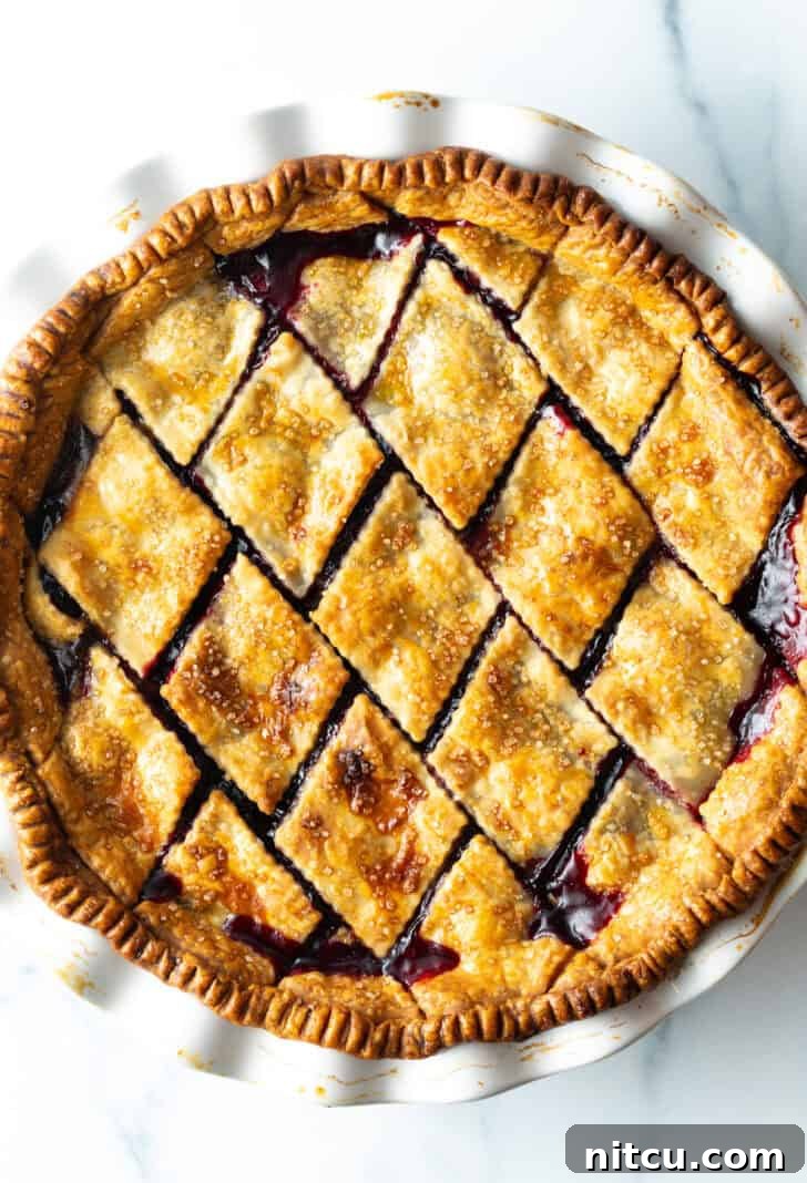 A beautifully baked cherry pie, featuring a golden, intricately patterned diamond crust, showcases the rich, homemade cherry pie filling beneath.