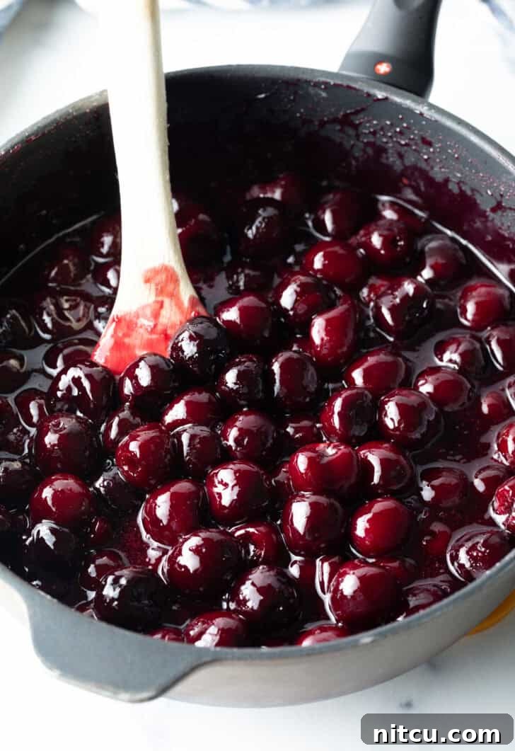 Homemade cherry pie filling simmering gently in a large pot, with a wooden spoon stirring the vibrant red mixture, showing the filling in its cooking process.