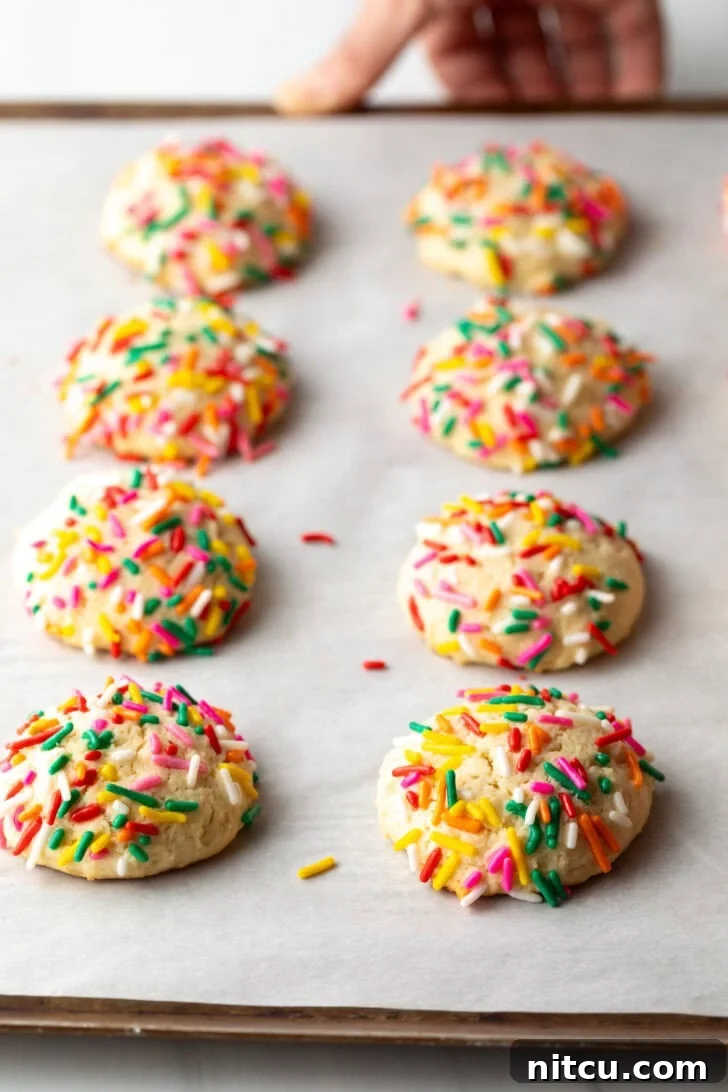 8 cream cheese cookies on a baking sheet, each topped with sprinkles.