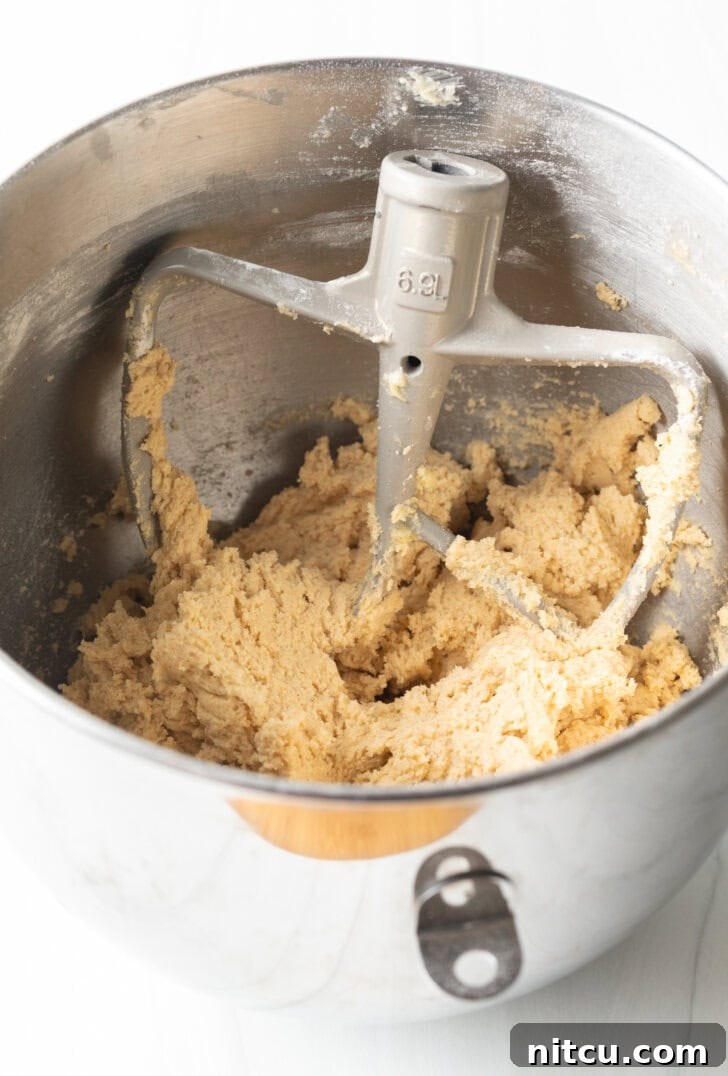 A stand mixer actively mixing cookie dough in a large bowl, showcasing the creaming process.