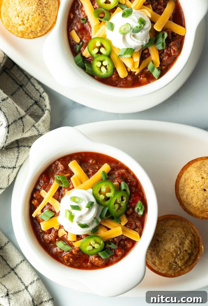 Top down view of a white bowl of beanless chili con carne topped with shredded cheese, jalapeno slices, sour cream and chopped green onions.