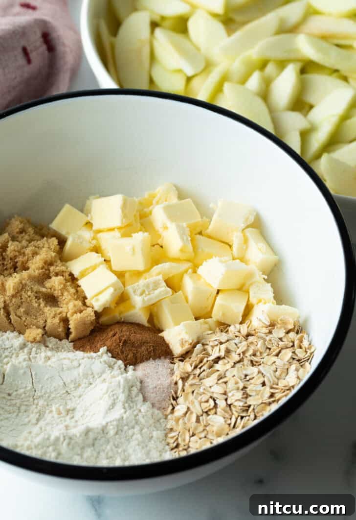 White bowl with flour, cubes of butter, brown sugar, oats, and spices, ingredients for apple crisp topping.