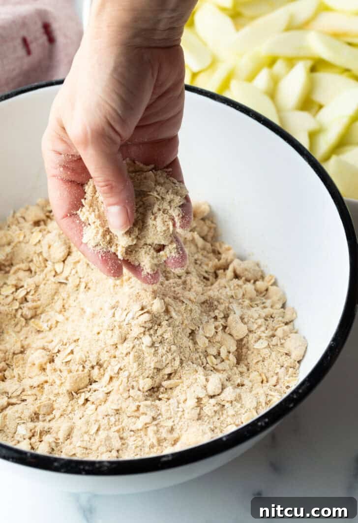 Hand mixing oat crumbly topping in a white bowl, showing the texture of the crisp topping.