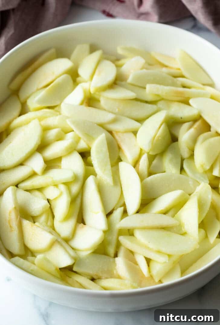White oval baking dish filled with thinly sliced apples, prepared for apple crisp filling.