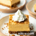 Square of pumpkin pie cheesecake on a white plate, topped with whipped cream.