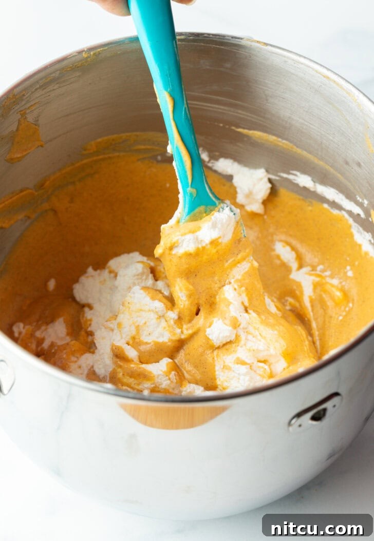 Pumpkin puree and cream cheese being mixed together with a blue spatula in a large metal bowl.