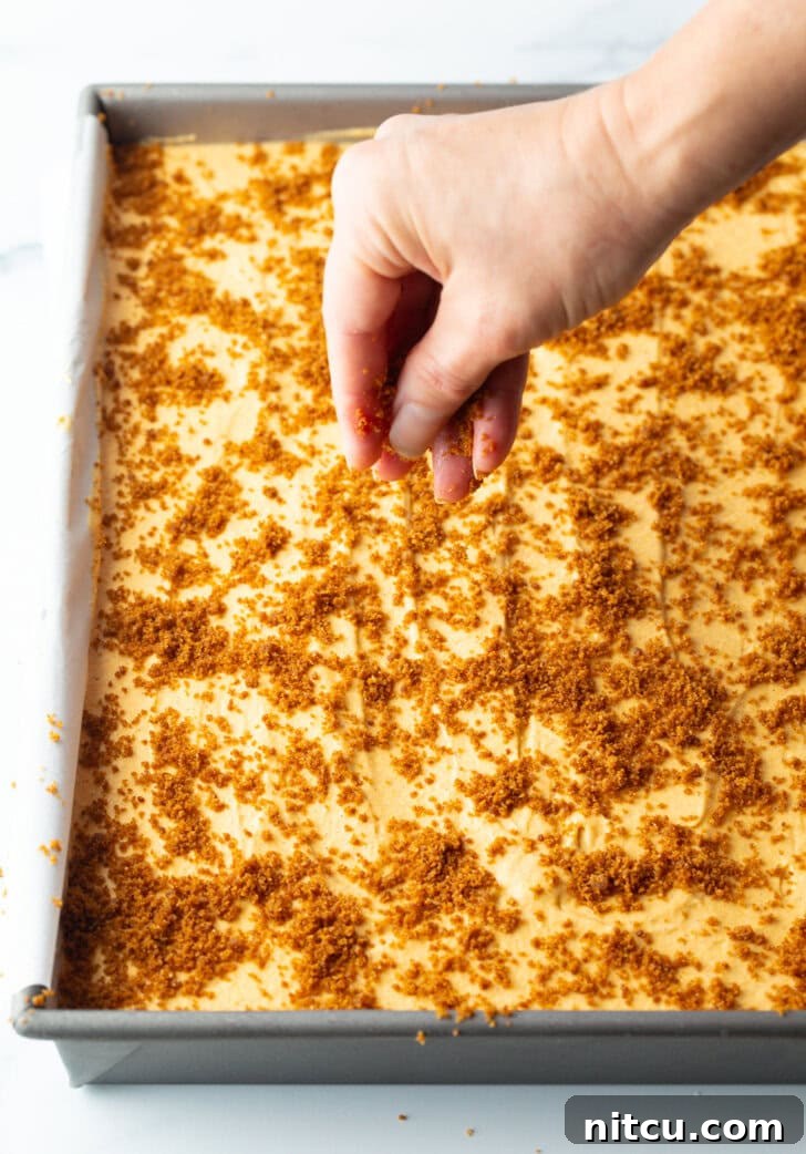 Hand adding crumbled cookie bites of the top of the cheesecake.