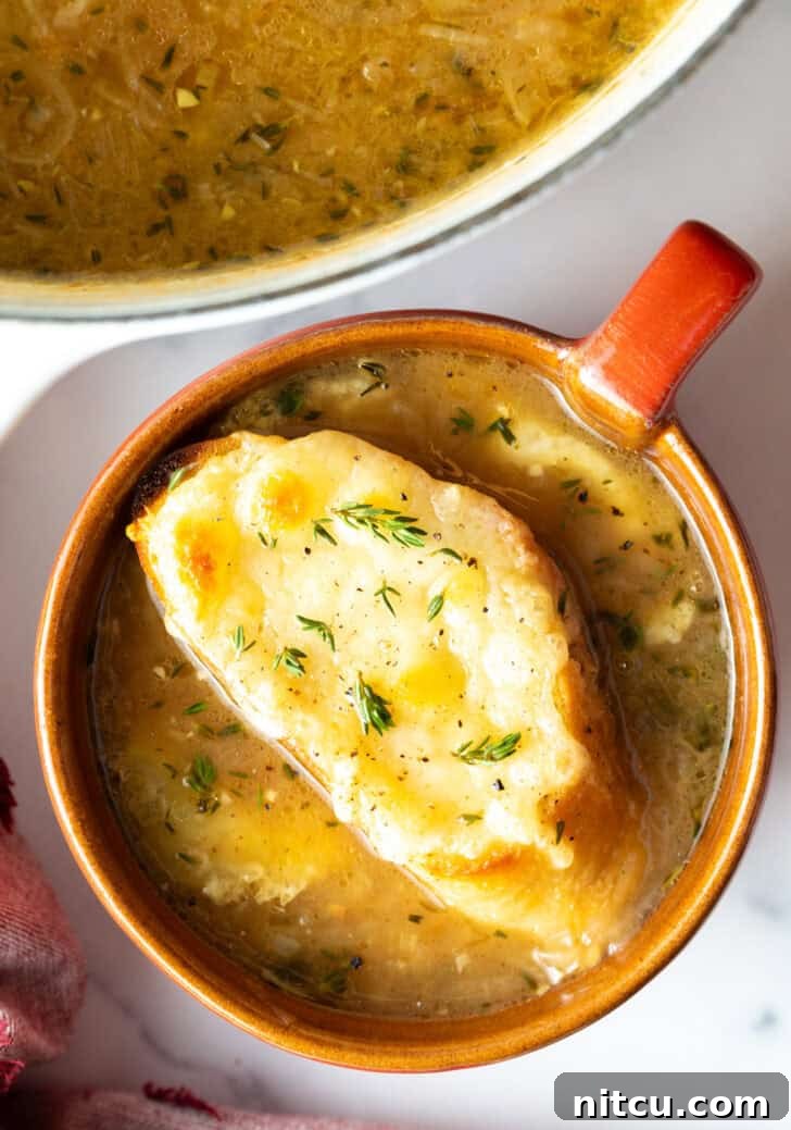 Top down view of a large red mug with French onion soup, topped with a slice of baguette with melted cheese.