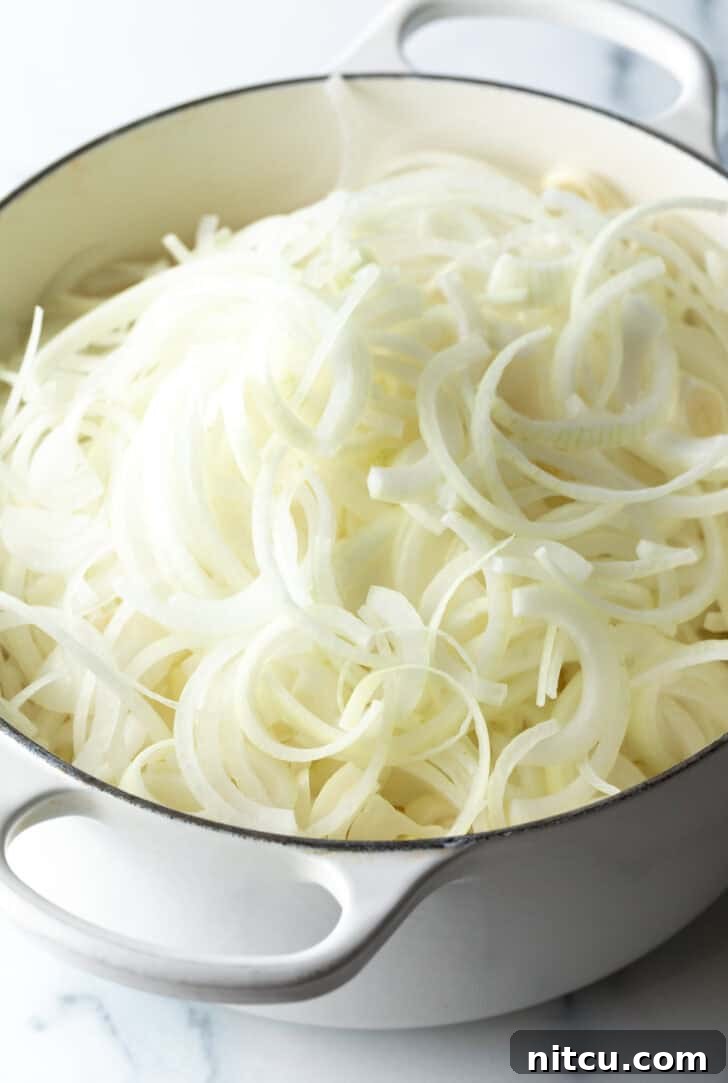 Large white cooking pot brimming with thinly sliced white onions.