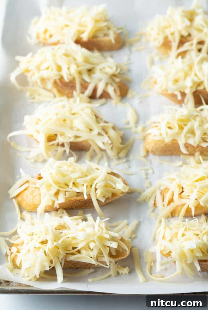 8 slices of baguette topped with shredded cheese, ready for broiling.
