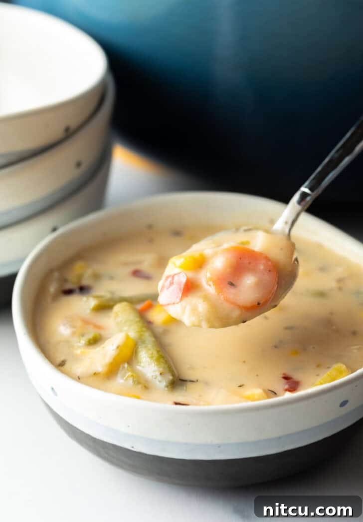 A bowl of cream veggie soup, with a spoon showing a scoop above the bowl.