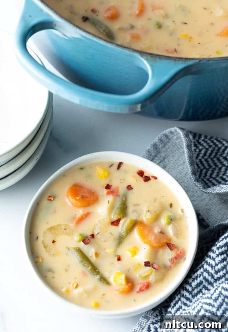 Top down bowl of creamy vegetable soup with carrots, green beans, corn, and potatoes.